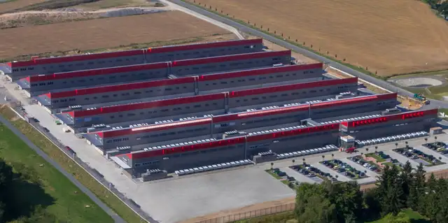 Aerial view of long rows of low datacenter halls with red stripes, in fields outside Falkenstein.
